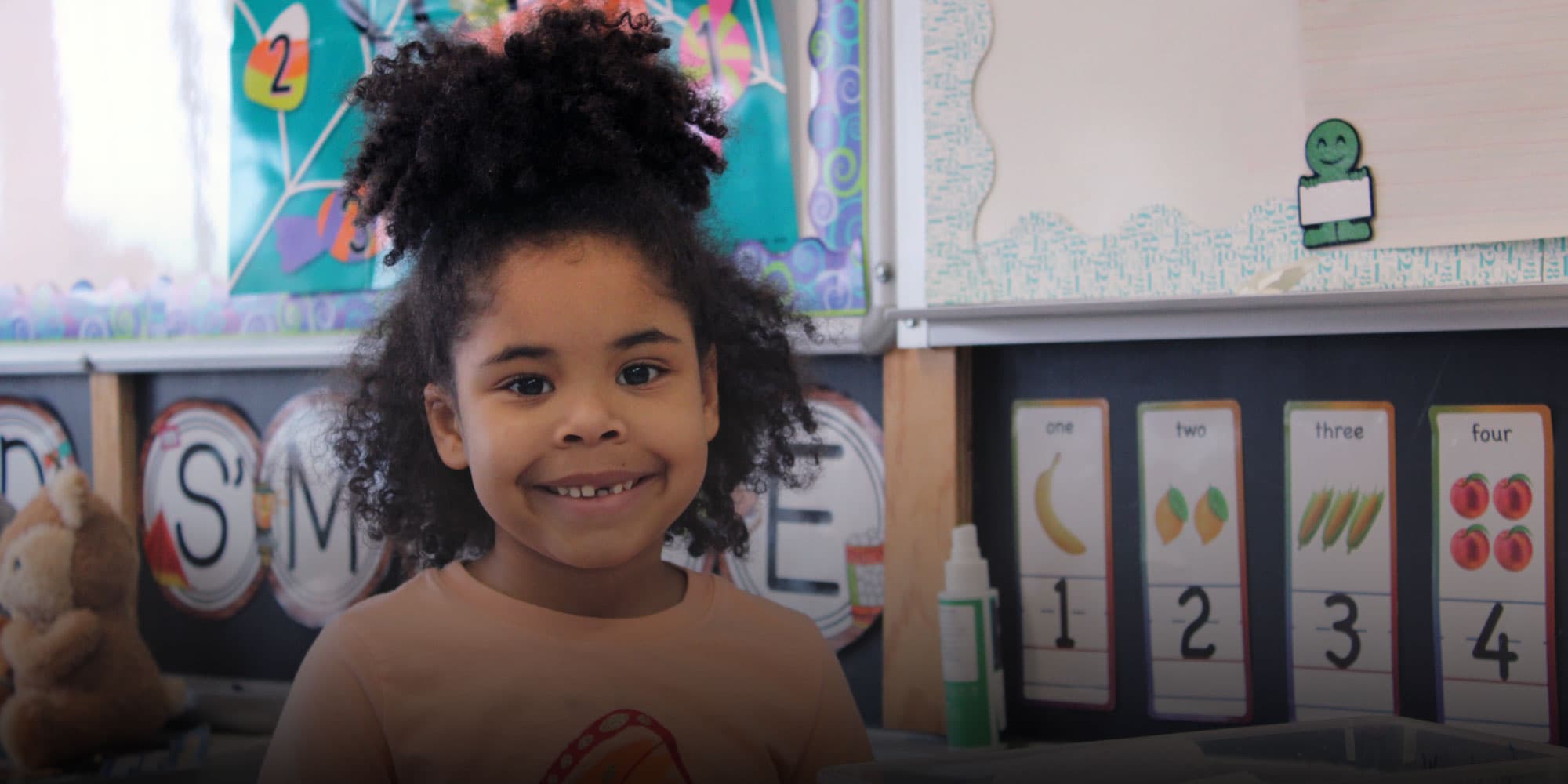 Smiling student with curly hair in a Bridges Prep classroom.